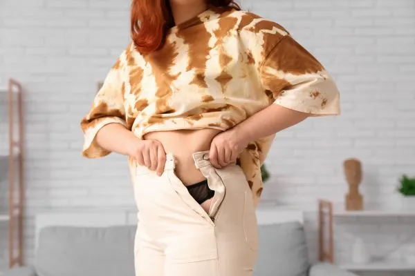 Image of woman trying to do her trousers up after pregnancy weight gain Spring Bank